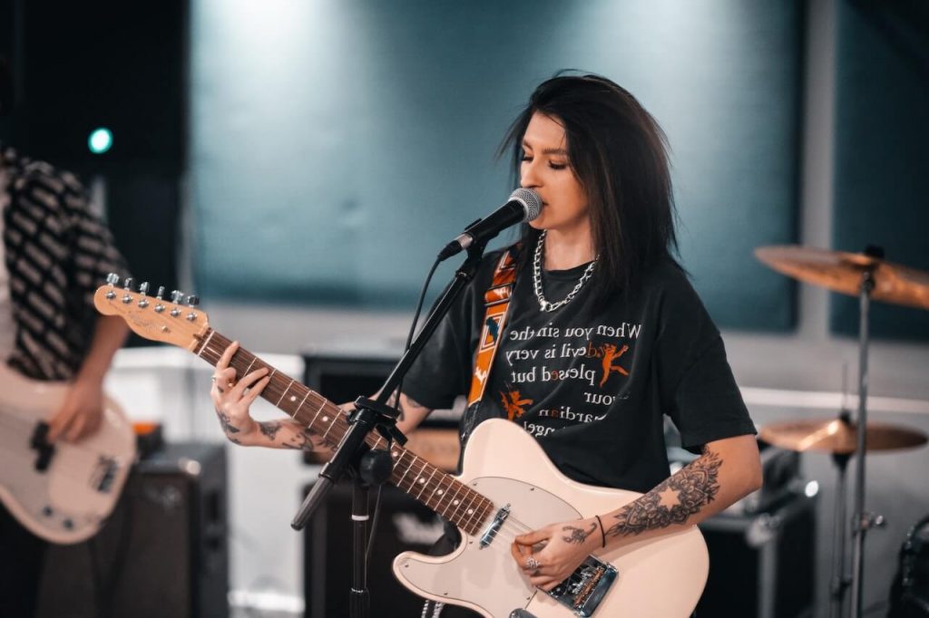 Un'immagine di una ragazza tatuata che canta appassionatamente in un microfono mentre suona la chitarra.